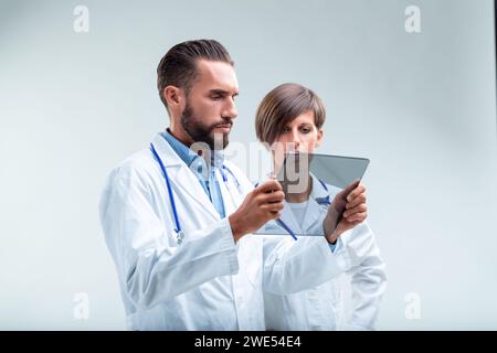 Medical professionals engage with advanced technology, analyzing data on a transparent tablet, focused and critical Stock Photo