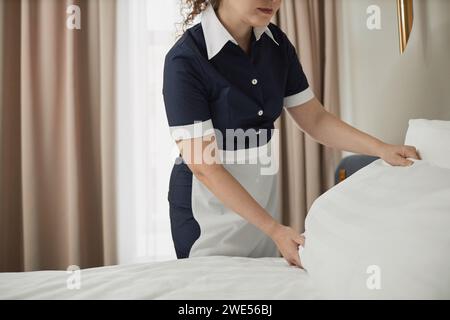 Close up of unrecognizable young maid adjusting pillows on hotel room bed with white sheets, copy space Stock Photo