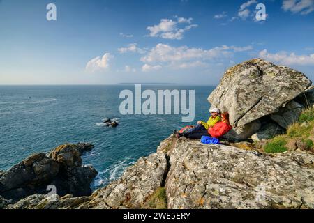 Man and woman hiking sitting on rocks and looking at the coast, Cap-Sizun, GR 34, Zöllnerweg, Brittany, France Stock Photo