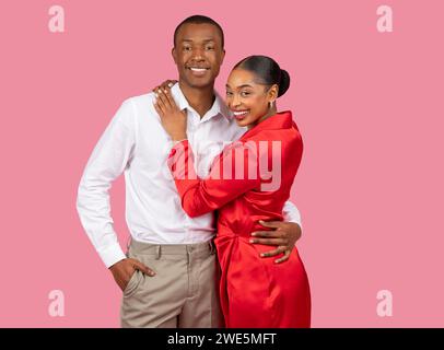 Smiling black couple embracing, woman in red dress, man in white shirt, pink background Stock Photo