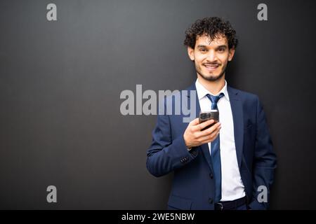 Smiling businessman using his cellphone in front of a dark wall Stock Photo