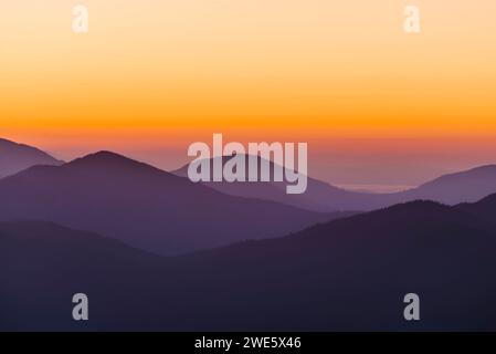 Silhouette of mountain ranges in haze with dramatic sunrise sky. Soft focus. Stock Photo