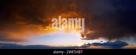 Dramatic sunset sky with dark rainy clouds illuminated with sun. Natural background of cloudy sky. Stock Photo