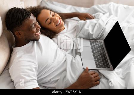 Happy young black couple relaxing in bed using laptop indoor Stock Photo