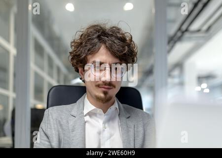 Professional young male executive working attentively at his desk in a well-lit office space, exuding confidence and concentration in his corporate role. Stock Photo