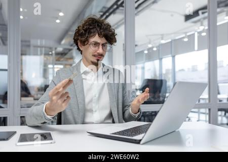 A young adult businessman is shown feeling perplexed at his workplace, a modern office, suggesting the challenges of problem-solving and decision-making that office workers often face. Stock Photo