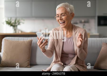 Cheerful senior woman using smartphone and having fun at home Stock Photo
