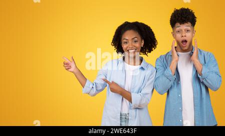 Surprised young man with hands on cheeks and smiling young woman pointing to the side Stock Photo