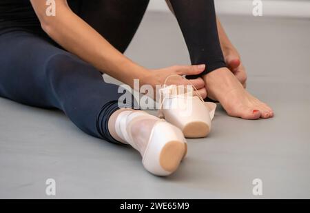 Ballet dancer putting on shoes at start of practice session in dance studio. Stock Photo
