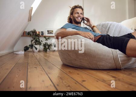 Smiling young man relaxing in beanbag at home talking on the phone Stock Photo