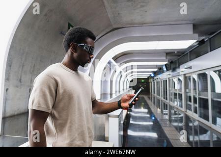 Man wearing futuristic glasses standing at metro station using smartphone Stock Photo