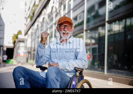 Happy senior man showing fist sitting in wheelchair Stock Photo