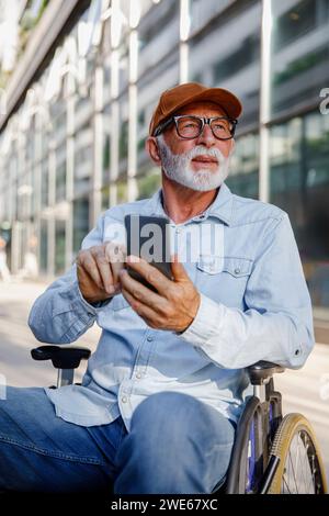 Retired senior man using smart phone sitting in wheelchair Stock Photo