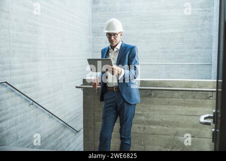 Senior engineer wearing hardhat and using tablet PC near wall Stock Photo