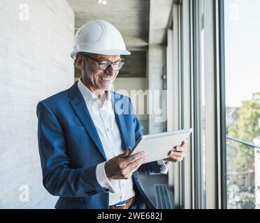 Happy senior engineer using tablet PC near window in corridor Stock Photo