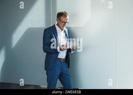 Businessman using tablet PC and leaning on wall Stock Photo