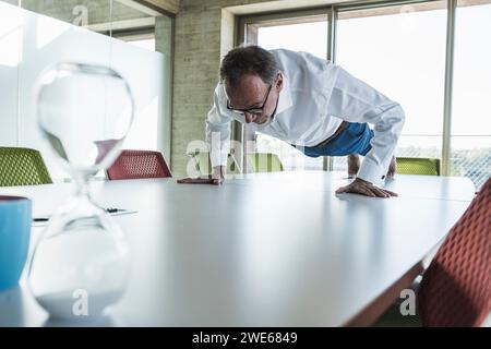 Senior businessman doing push-ups on desk in office Stock Photo