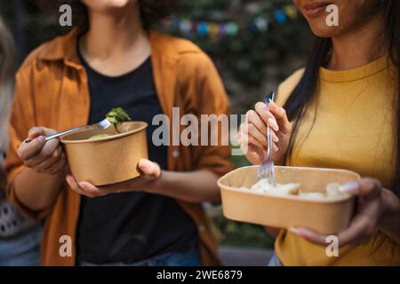 Happy friends eating together in garden from disposable containers Stock Photo