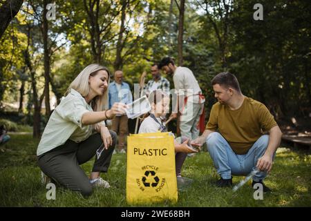 Socially inclusive group of volunteers putting plastic waste in recycling bag Stock Photo