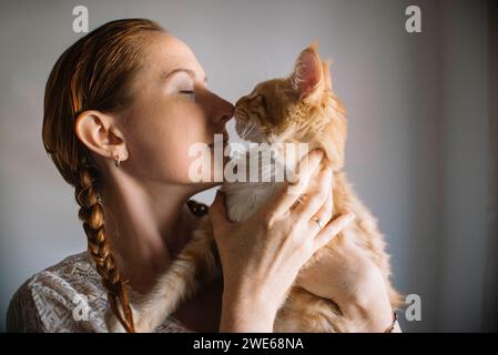 Redhead woman embracing ginger cat at home Stock Photo