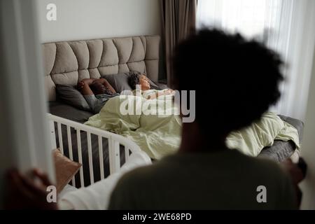 Boy looking at his parents sleeping on bed in bedroom at home Stock Photo