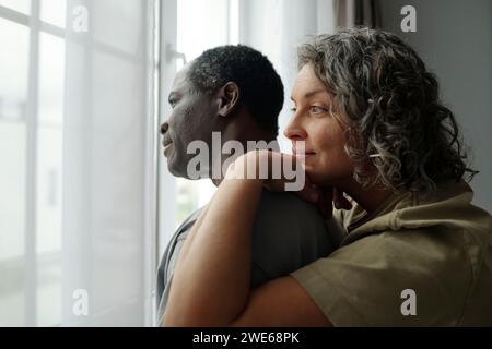 Multiracial mature couple looking through window at home Stock Photo