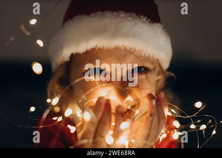 Happy girl wearing Santa hat and holding string lights in hand Stock Photo
