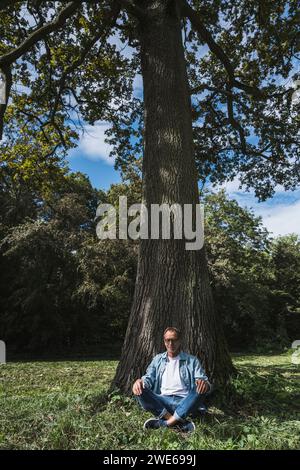 Senior man practicing yoga sitting on grass in park Stock Photo