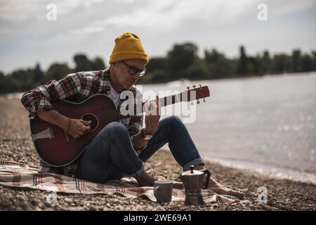 Senior man playing guitar sitting by sea on weekend Stock Photo