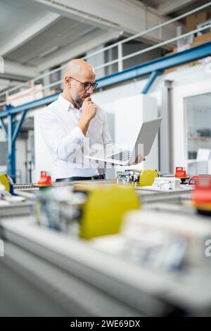 Businessman planning and using laptop near machinery in factory Stock Photo