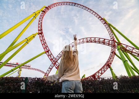 Young woman gesturing peace sign in front of rollercoaster Stock Photo