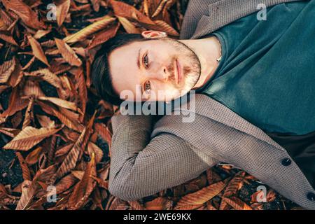 Smiling young man relaxing on autumn leaves Stock Photo