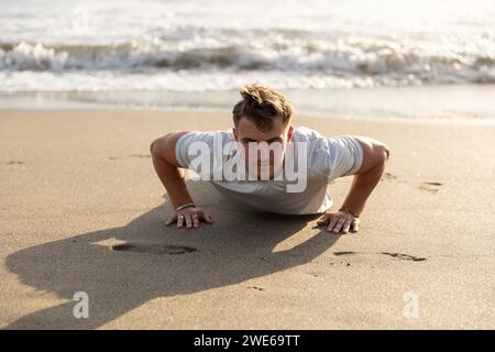 Man doing push-ups on sand at beach Stock Photo