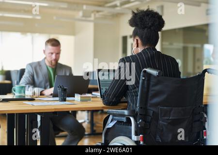 Businesswoman in wheelchair working on laptop with coworker in office Stock Photo