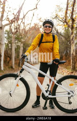 Smiling woman standing with mountain bike on road in forest Stock Photo