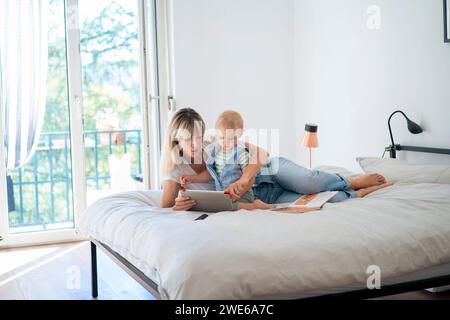 Mother lying on bed and using tablet PC with son at home Stock Photo