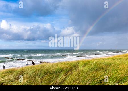 Germany, Mecklenburg-Vorpommern, Grassy beach with rainbow arching against cloudy sky over sea in background Stock Photo