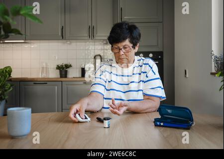 Senior woman measuring blood sugar with glucometer in kitchen Stock Photo