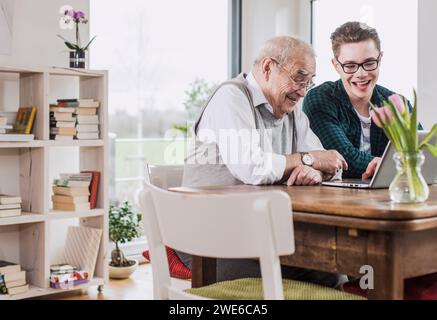 Happy young man teaching laptop to grandfather at home Stock Photo