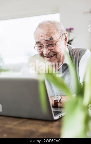 Smiling senior man talking on video call through laptop at home Stock Photo