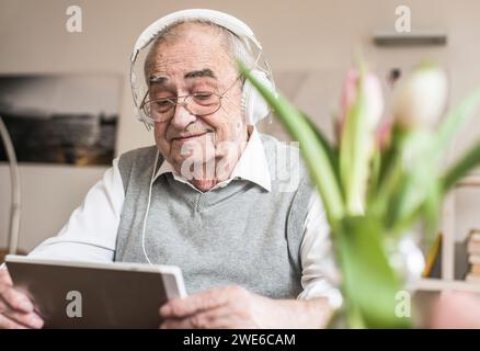 Smiling senior man wearing headphones and using tablet PC at home Stock Photo