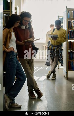 Students standing near shelves and reading books in library Stock Photo