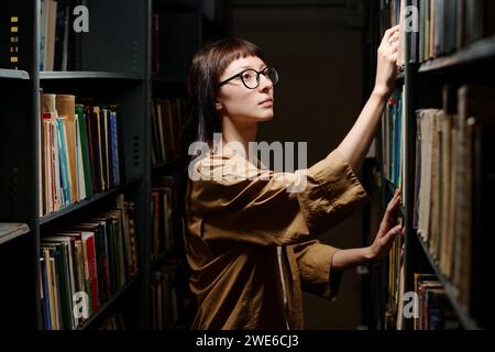 Young student taking book from top shelf in library Stock Photo
