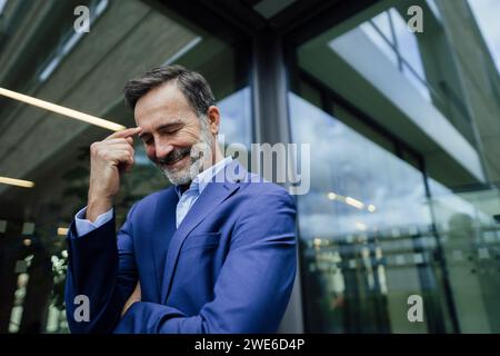 Smiling businessman touching forehead with finger in office Stock Photo