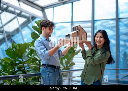 Smiling multiracial architects with model house standing in corridor Stock Photo