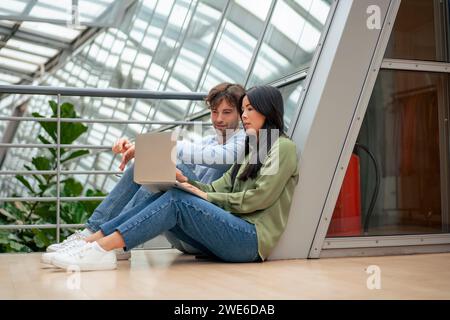 Multiracial colleagues using laptop sitting in corridor of office Stock Photo