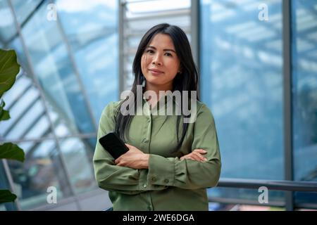 Confident businesswoman with smart phone in corridor Stock Photo