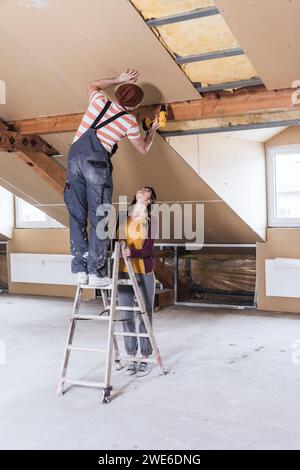 Man standing on ladder and drilling wall with woman at home Stock Photo