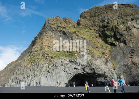 Tourists stroll on Reynisfjöru beach with Reynisdrangar stacks and cave called Hálsanefshellir in the background. Stock Photo