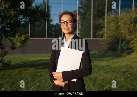 Smiling businesswoman standing with file folder in office park Stock Photo